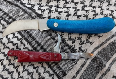 On top is a pruning knife with a blue plastic handle. Sturdy construction, strong spring. Handle is labeled "HM", a logo of a vine and the price of 1 ruble and 35 kopeks. Below is a little penknife by the Red October factory in Vorsma. They use a Rooster logo. According to folks I asked, that little hooked blade is supposed to be a can opener. It's a decently built knife with strong springs, but I wouldn't want to attempt to open any cans with that thing.