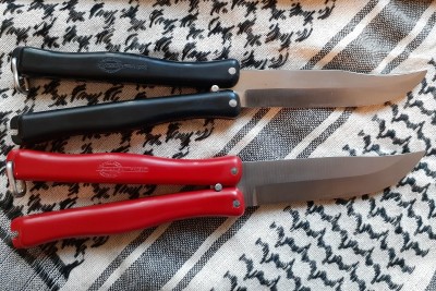 The style of the logo is identical, reading "Hackman Finland" and with "Stainless Sorsakoski" in the roundel. The blade on the black example has a more pronounced clip point than the puukko styled blade of the red version.